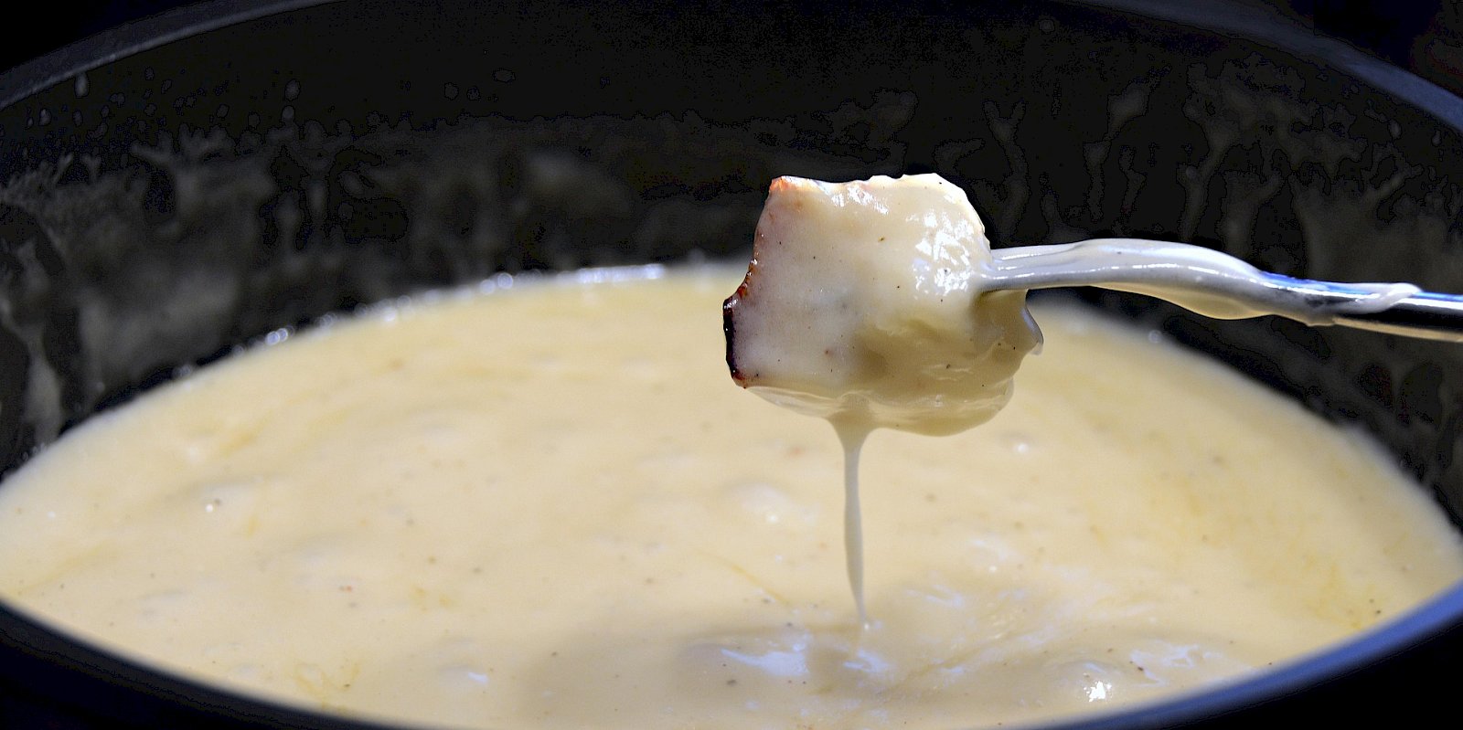 Ein Stück Brot wird mit der Gabel aus einem Käsefondue gezogen